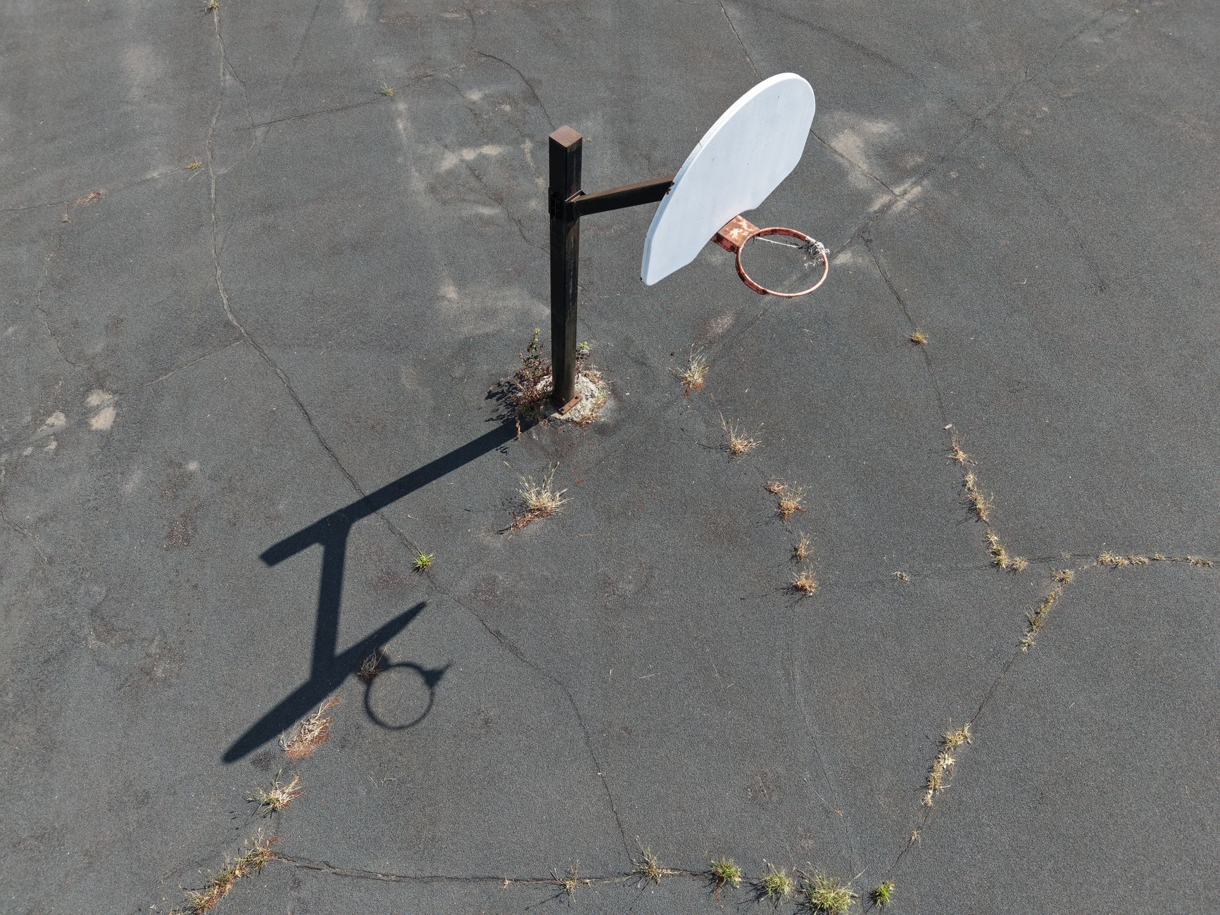 Aerial view of an old, neglected basketball hoop on a cracked asphalt court.