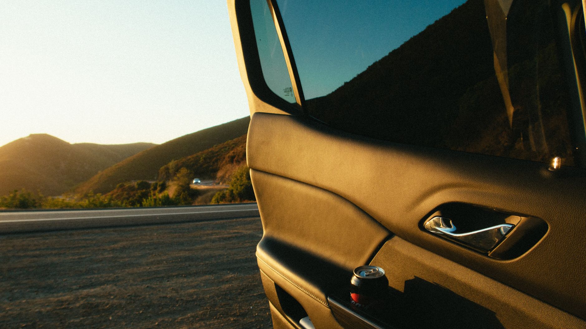 View of an open car door with a scenic road and sunset in the background, capturing a tranquil travel moment.