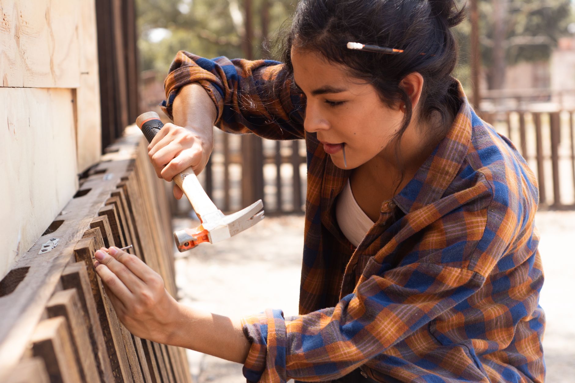 A worker uses a hammer to repair a wooden fence.